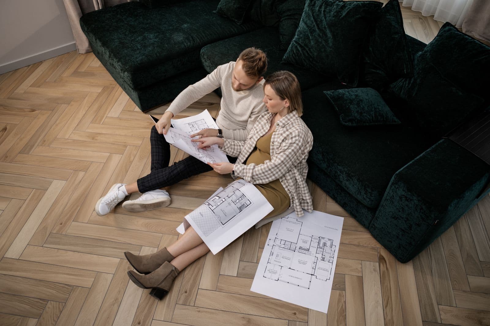 Un couple étudie les plans d'un logement, assis au sol de son salon